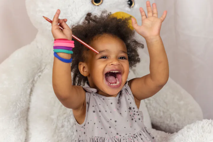 A toddler laughing, both arms in the air.